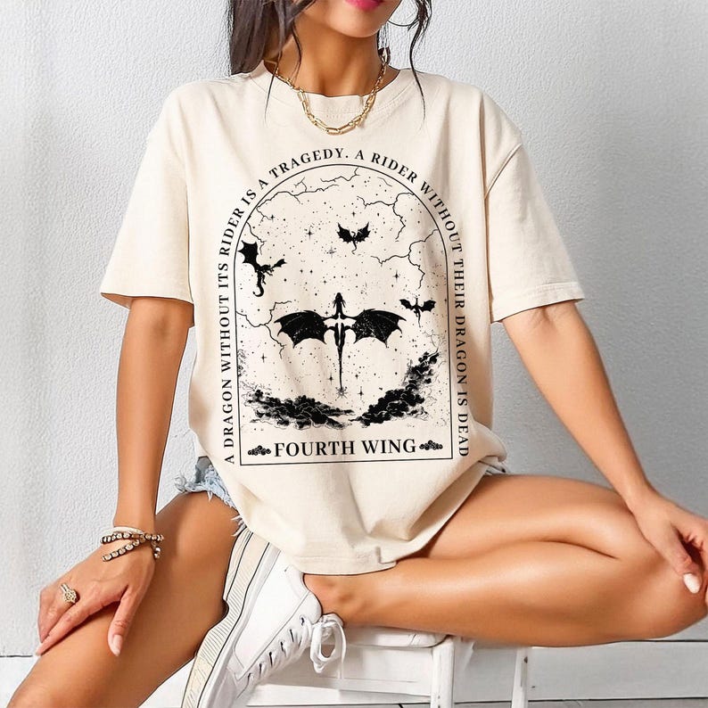May include: A beige t-shirt with a black graphic print of a dragon and the text "A tragedy. A rider without their dragon is dead. A dragon without its rider is a fourth wing."