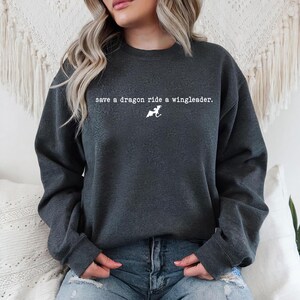 May include: A dark gray sweatshirt with the text "save a dragon ride a wingleader." printed in white. A white silhouette of a dragon is also printed on the sweatshirt.
