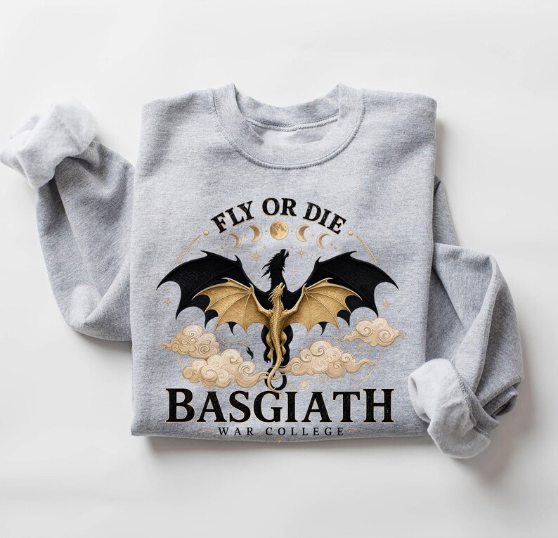 May include: A light gray sweatshirt featuring a dragon design with the text "FLY OR DIE" above and "BASGIATH WAR COLLEGE" below. The dragon has black and gold wings, with a full moon and clouds in the background.