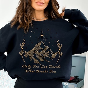 May include: Black sweatshirt with a gold graphic of mountains, stars, and the text "Only You Can Decide What Breaks You."