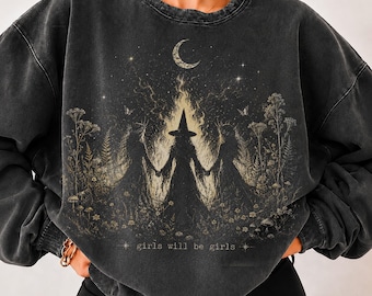 Op de afbeelding: Een antracietgrijze sweater met ronde hals en een grafische print van drie figuren met puntmutsen die elkaars hand vasthouden tussen hoge wilde bloemen en vlammen. Boven hen bevinden zich een maansikkel en sterren.