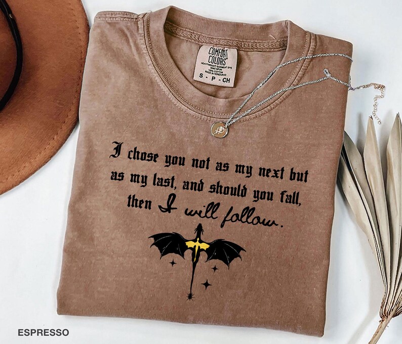 May include: Espresso-colored t-shirt with the text "I chose you not as my next but as my last, and should you fall, then I will follow." A black dragon graphic with yellow accents is below the text. A silver necklace is draped across the shirt.