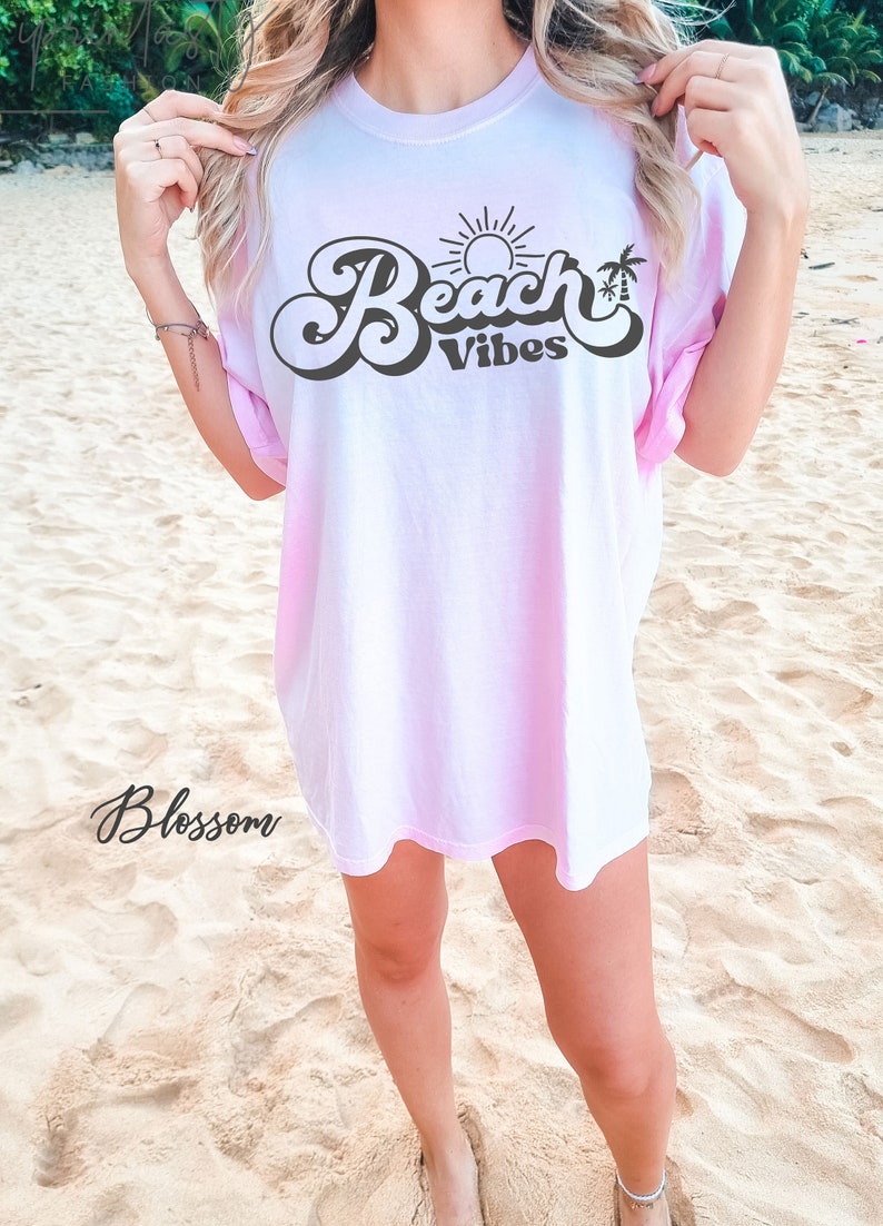 May include: A pink tie-dye t-shirt with the text "Beach Vibes" in a retro font. The text is in black and features a sun and palm tree graphic.