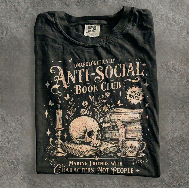 May include: Black t-shirt with a graphic design featuring a skull, books, a candle, and a teacup. The text reads "UNAPOLOGETICALLY ANTI-SOCIAL BOOK CLUB" and "MAKING FRIENDS WITH CHARACTERS, NOT PEOPLE."