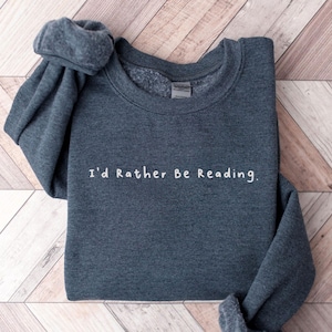 K&ouml;nnte beinhalten: Ein dunkelgrauer Pullover mit dem Aufdruck "I'd Rather Be Reading." in Wei&szlig; auf der Vorderseite.