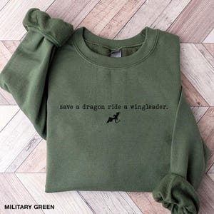 May include: A military green sweatshirt with the text "save a dragon ride a wingleader." and a small black silhouette of a dragon.