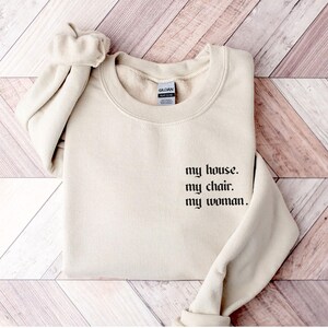 May include: A cream-colored sweatshirt with the text "my house. my chair. my woman." printed in black.