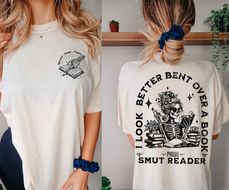 May include: A white t-shirt with a black graphic of a skeleton reading a book. The text on the shirt reads "I look better bent over a book, Proud Smut Reader".