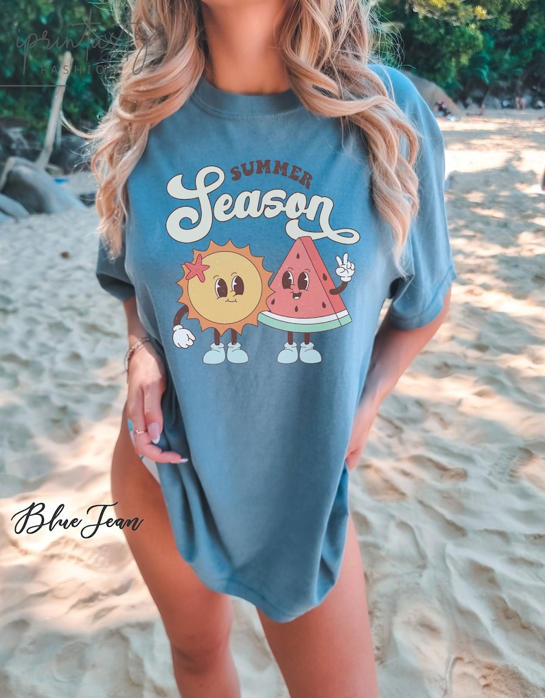 May include: A blue t-shirt with a graphic of a smiling sun and watermelon with the text "Summer Season".