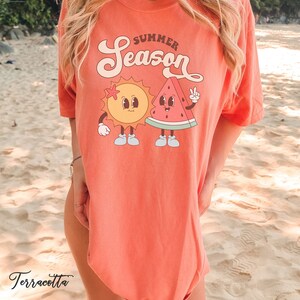 May include: A terracotta colored t-shirt with a graphic of a smiling sun and watermelon with the text "Summer Season" on the front.