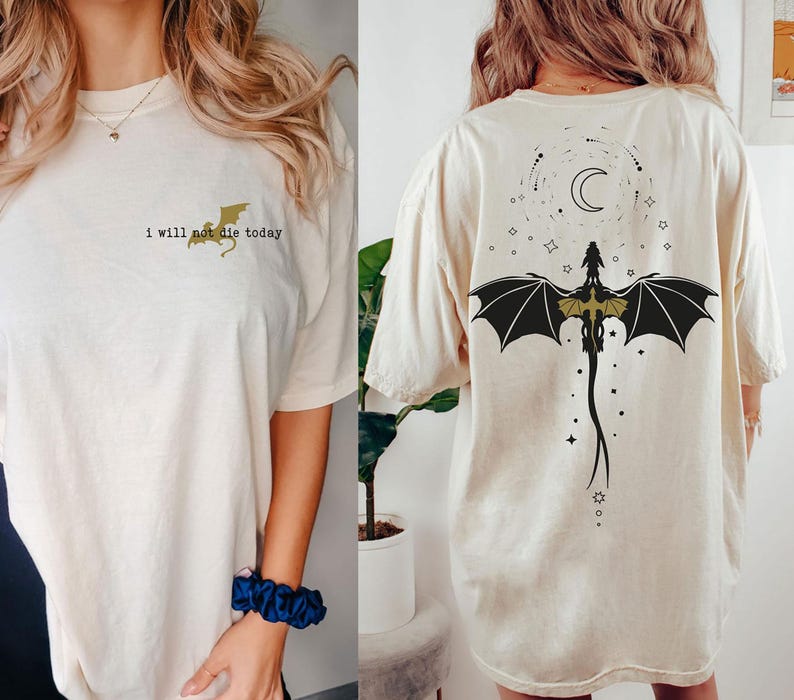 Puede incluir: Una camiseta blanca con un gr&aacute;fico de drag&oacute;n dorado y el texto "I will not die today" en la parte delantera. La parte posterior de la camiseta presenta un gr&aacute;fico de drag&oacute;n negro con una luna creciente y estrellas.