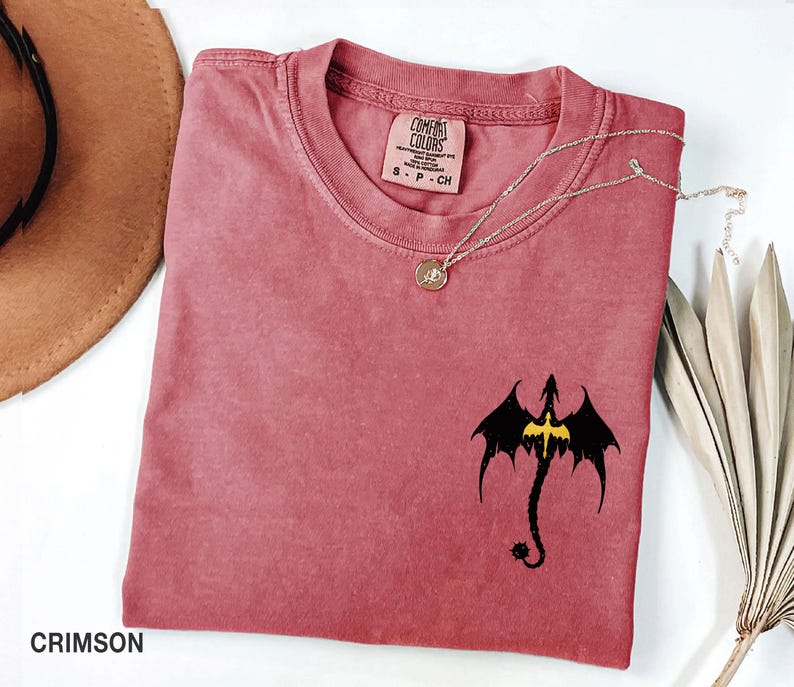 May include: Crimson red t-shirt with a black dragon silhouette with yellow accents. The shirt is made by Comfort Colors and has a tag that says "S - P - CH".