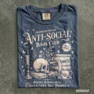 May include: Midnight blue t-shirt with the text "Unapologetically Anti-Social Book Club" and illustrations of a skull, books, a candle, and a teacup. The shirt also has the text "Making Friends With Characters, Not People."