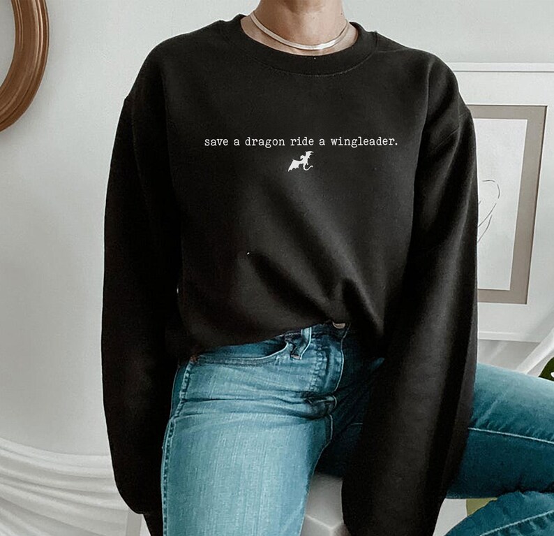 May include: Black sweatshirt with the text "save a dragon ride a wingleader." and a small graphic of a dragon. The model is wearing blue jeans.
