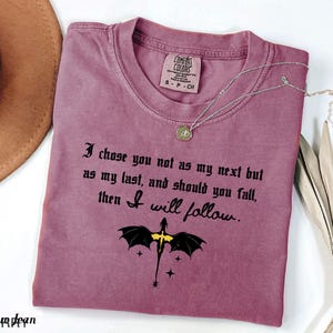 May include: A mauve Comfort Colors t-shirt with the text "I chose you not as my next but as my last, and should you fall, then I will follow." A dragon graphic is below the text. A silver necklace is on the shirt.
