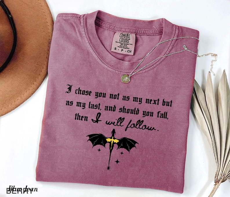 May include: A mauve Comfort Colors t-shirt with the text "I chose you not as my next but as my last, and should you fall, then I will follow." A dragon graphic is below the text. A silver necklace is on the shirt.
