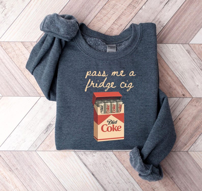 May include: A navy blue sweatshirt with the text "pass me a fridge cig" in a cursive font. Below the text is a graphic of a Diet Coke box with Diet Coke cans inside.