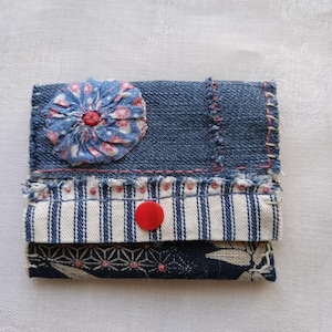 May include: A small blue and white fabric wallet with a red button and a blue and pink fabric flower.