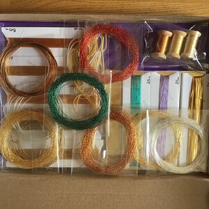 May include: A box of assorted metallic embroidery threads in various colors, including gold, silver, copper, and green. The threads are packaged in clear plastic bags and labeled with the length in inches. The box also includes three spools of gold thread.