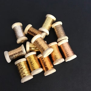 May include: A collection of spools of metallic thread in gold, silver, and copper colours. The spools are made of wood and have a variety of textures.