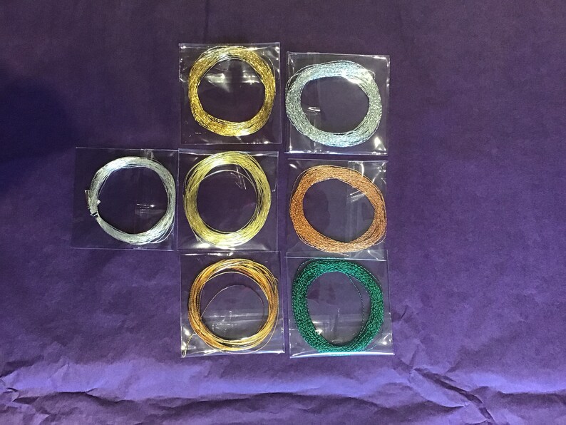 May include: Eight spools of metallic thread in various colors, including gold, silver, copper, and green, are displayed in clear plastic packaging.