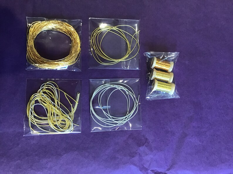 May include: Five clear plastic bags containing spools of gold and silver wire. The wire is in various thicknesses and is arranged in a variety of ways. The bags are on a purple surface.