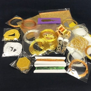 May include: Assortment of gold and white craft supplies in clear plastic bags. The supplies include wire, thread, beads, and a honeycomb-shaped block of wax.