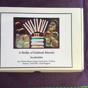 May include: A white box with a picture of goldwork materials, including wire, thread, and beads. The box is labeled "A Medley of Goldwork Materials" and "Arcadianbliss". The address of the seller is also included on the box.
