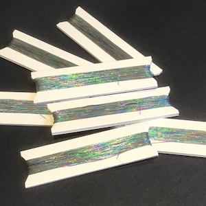 May include: Six spools of iridescent thread on white cardboard spools. The thread is a mix of silver, green, and blue.