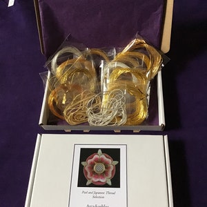 May include: A white box with a purple fabric lining. The box contains a variety of gold and silver threads, along with a card that reads "Purl and Japanese Thread Selection Arcadianbliss Joe Walden, Manor Cottage, Church Street, Winsham, Somerset, TA20 4EU, United Kingdom".