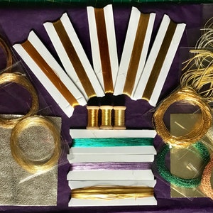 May include: Assortment of gold, silver, and copper metallic threads and cords in various sizes and textures. The threads are packaged in clear plastic bags and spools. There are also two sheets of metallic paper.