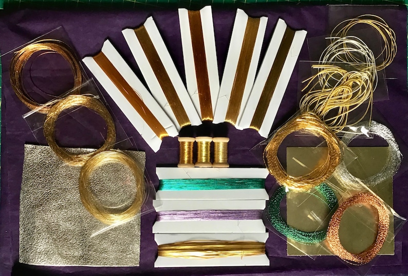 May include: Assortment of gold, silver, and copper metallic threads and cords in various sizes and textures. The threads are packaged in clear plastic bags and spools. There are also two sheets of metallic paper.