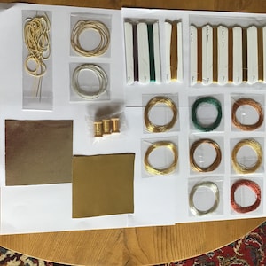 May include: Assortment of embroidery floss, thread, and needles in various colors, including gold, green, and copper. There are also two pieces of gold-colored fabric.