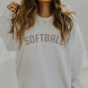 May include: White oversized sweatshirt with the word "SOFTBALL" printed in a distressed pink font.