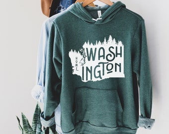 May include: A dark green hooded sweatshirt with a white graphic of the state of Washington, featuring the words "Home" and "Washington" inside the outline of the state. The graphic also includes a silhouette of trees.