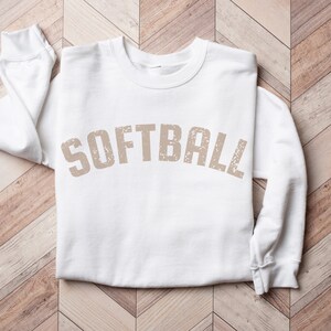 May include: White sweatshirt with the word "SOFTBALL" printed in a distressed brown font.