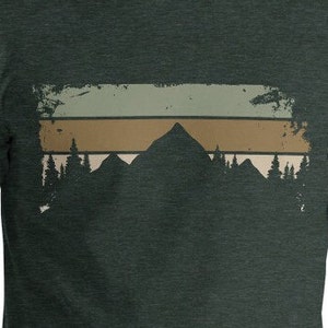 May include: A dark green t-shirt featuring a vintage-style graphic of a mountain range with a sunset behind it. The graphic has a faded, distressed look.