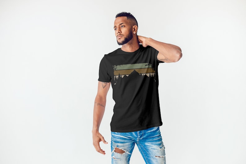 May include: A black t-shirt featuring a vintage-style graphic of mountains and trees in shades of green, brown, and beige.