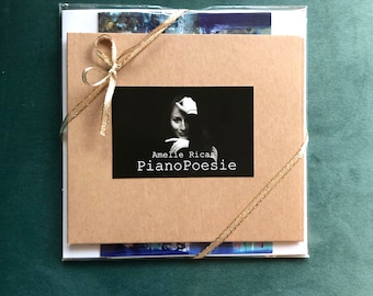 May include: A brown paper gift bag with a gold ribbon and a black and white photo card. The card features a woman with a hand on her face and the text "Amelie Ricas PianoPoesie".