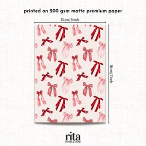 Może przedstawiać: Arkusz papieru do pakowania z powtarzającym się wzorem czerwonych i r&oacute;żowych kokardek. Papier jest drukowany na matowym papierze premium o gramaturze 200 g/m&sup2; i ma wymiary 13 cm x 18 cm.