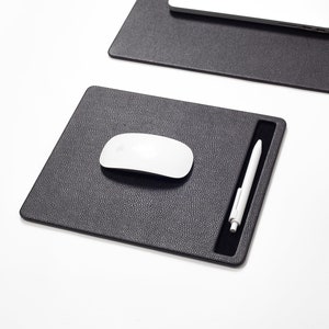 May include: A black leather desk mat with a built-in pen holder. A white wireless mouse is on the mat.