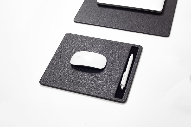 May include: A black leather desk mat with a built-in pen holder. A white wireless mouse is on the mat.