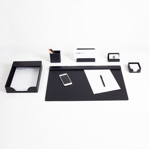 Könnte beinhalten: Schwarzes Leder-Schreibtisch-Organizer-Set mit Stifthalter, Visitenkartenhalter, Notizblockhalter und Telefonständer. Das Set befindet sich auf einer weißen Oberfläche.