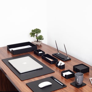May include: A black leather desk organizer set with a laptop, mouse pad, pen holder, and other office supplies. The set is on a wooden desk with a small bonsai tree in the background.