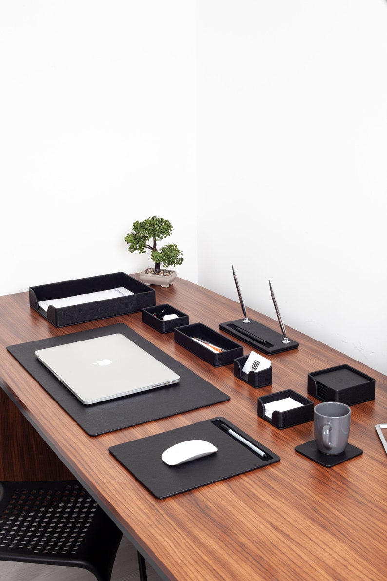 May include: A black leather desk organizer set with a laptop, mouse pad, pen holder, and other office supplies. The set is on a wooden desk with a small bonsai tree in the background.