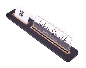 Könnte beinhalten: Schwarzer Leder-Schreibtisch-Namensschild mit Holz-Akzent und einem transparenten Acryl-Namensschildhalter. Das Namensschild lautet "John Smith, General Manager".