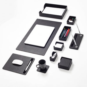 May include: A black desk organizer set with a variety of compartments and trays for pens, pencils, paper clips, and other office supplies. The set includes a mouse pad, a laptop mat, a pen holder, a cup holder, and a business card holder.