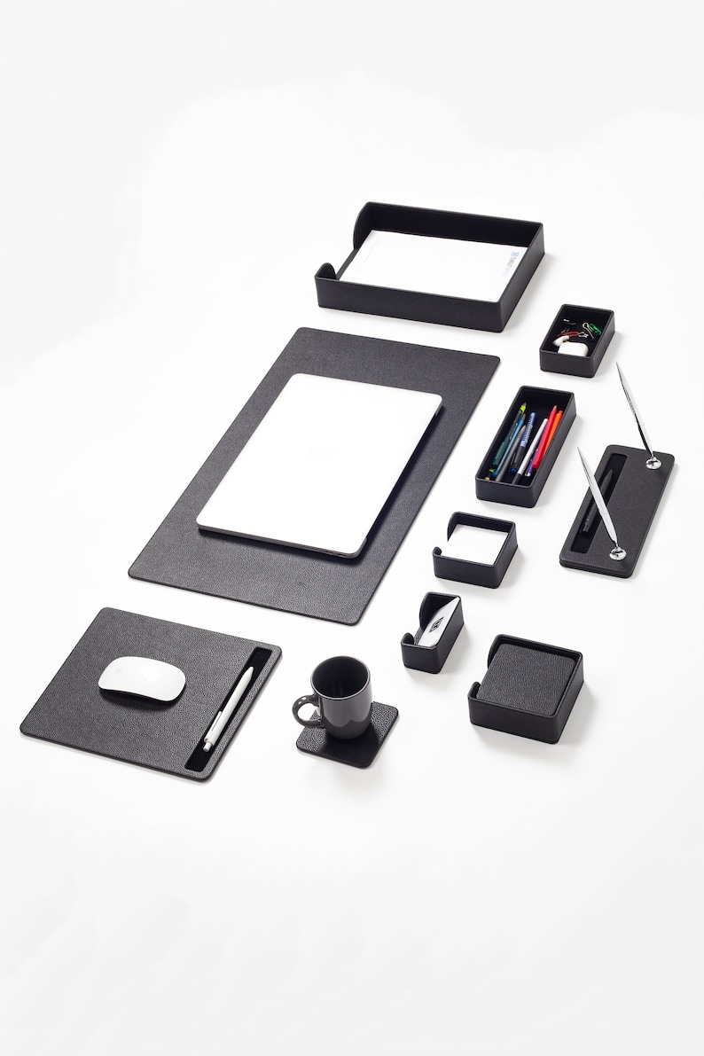 May include: A black desk organizer set with a variety of compartments and trays for pens, pencils, paper clips, and other office supplies. The set includes a mouse pad, a laptop mat, a pen holder, a cup holder, and a business card holder.