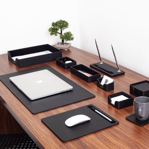 Peut inclure: Un ensemble d'organisateur de bureau en cuir noir avec un ordinateur portable, une souris, un porte-stylos et divers plateaux pour organiser les fournitures de bureau. L'ensemble est sur un bureau en bois.