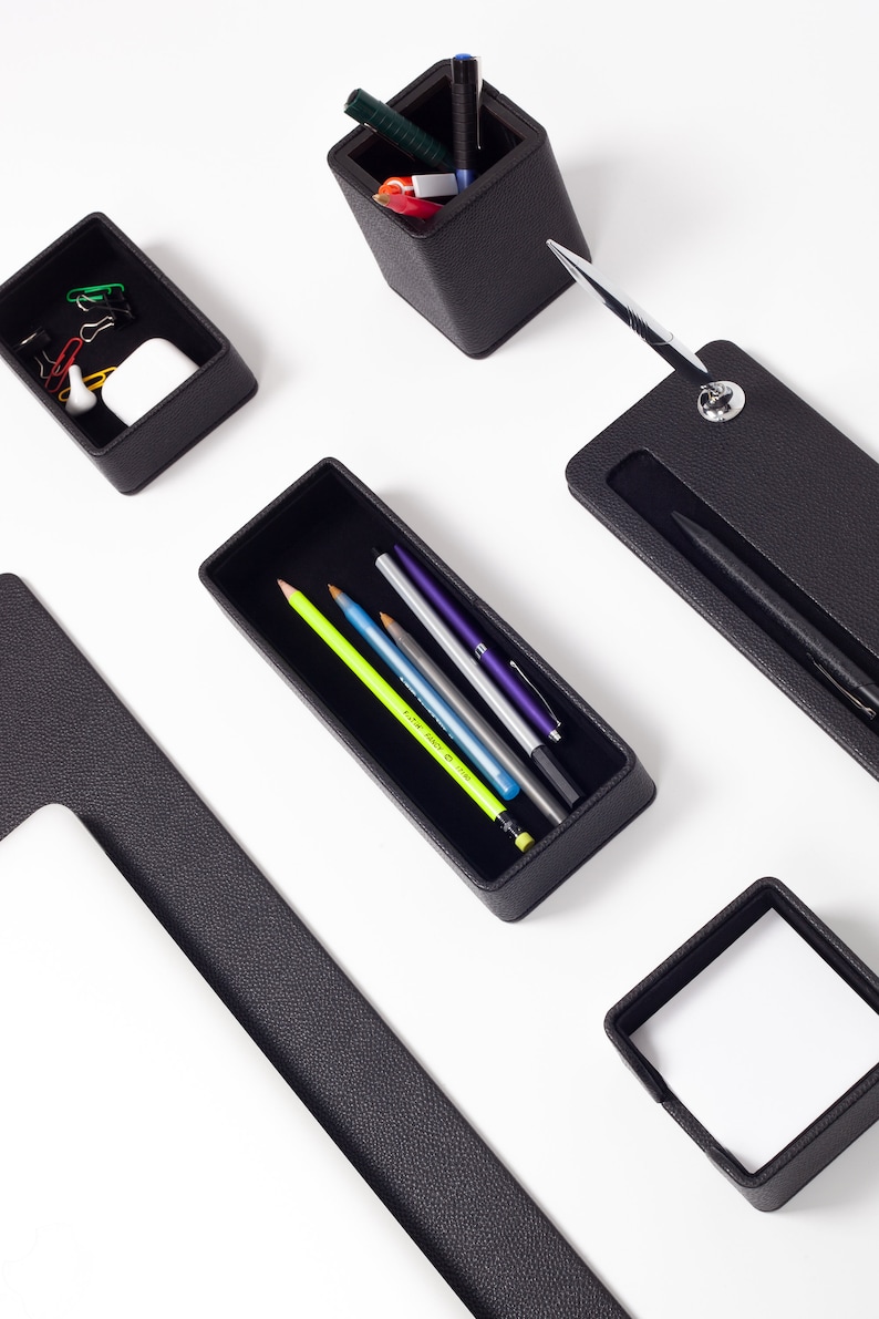 May include: Black leather desk organizer set with compartments for pens, pencils, and other office supplies. The set includes a pen holder, a pencil holder, a small tray, and a larger tray.